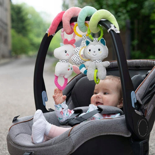 Spirala Fehn Aiko i Yuki na pałąku fotelika; dziecko sięga do jednej z zawieszek.