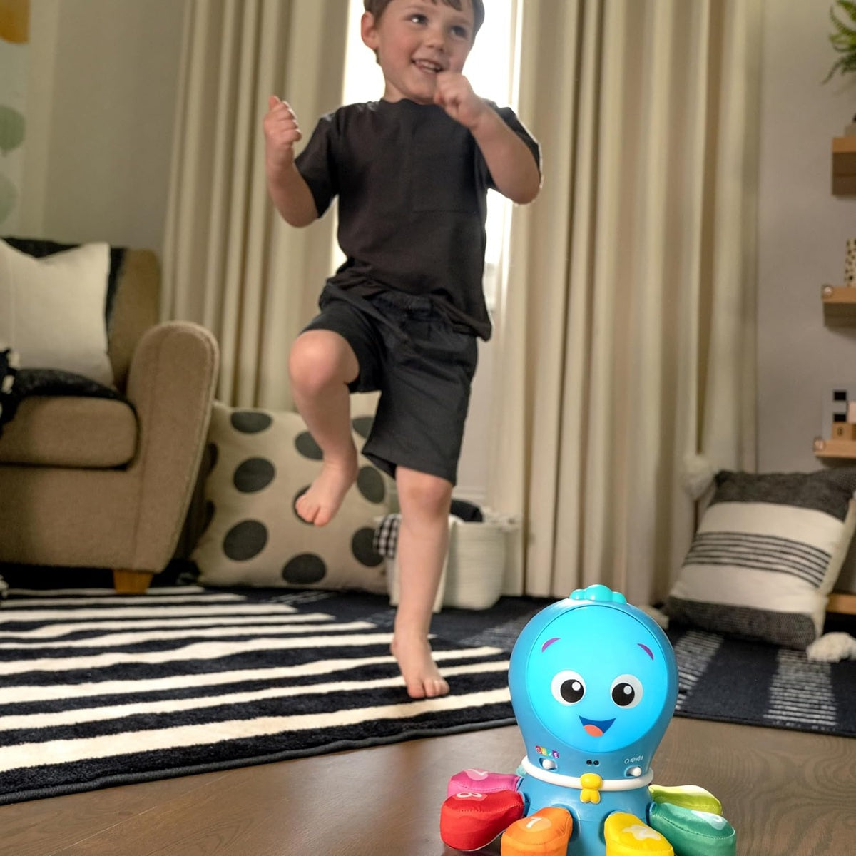 Chłopiec stojący przy dywanie obok niebieskiej ośmiornicy Baby Einstein Ocean Explorers.