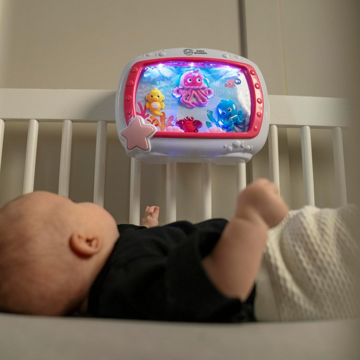 Dziecko wyciągające rękę w kierunku pozytywki Baby Einstein z morskim motywem na łóżeczku.