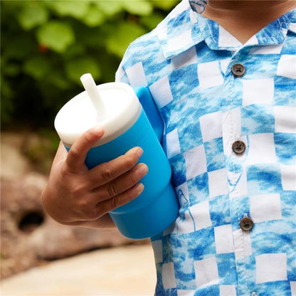 Zdjęcie poglądowe: dziecko trzyma niebieski kubek Infantino My 1st Tumbler z białą pokrywką i słomką; zbliżenie dłoni i kubka.